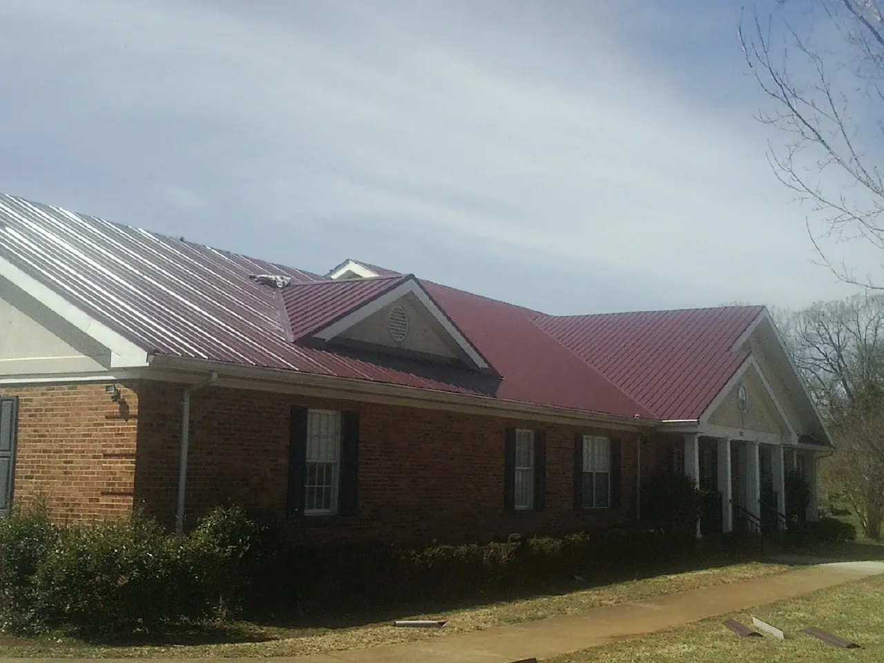 Red metal roof with gabled entries on a long brick building, from a Hail Damage Roof Repair job in Hyannis Port