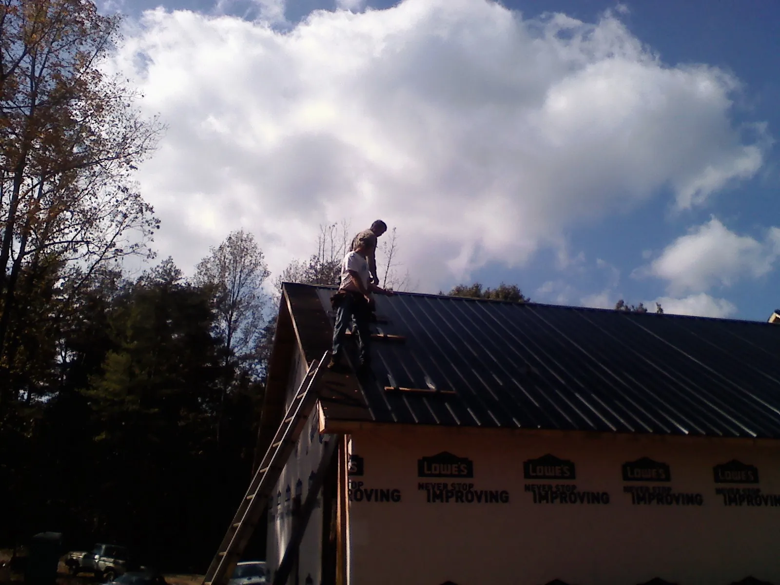 Roofer fastening dark metal panels high against a cloudy sky, from a Roof Inspection job in Hyannis Port