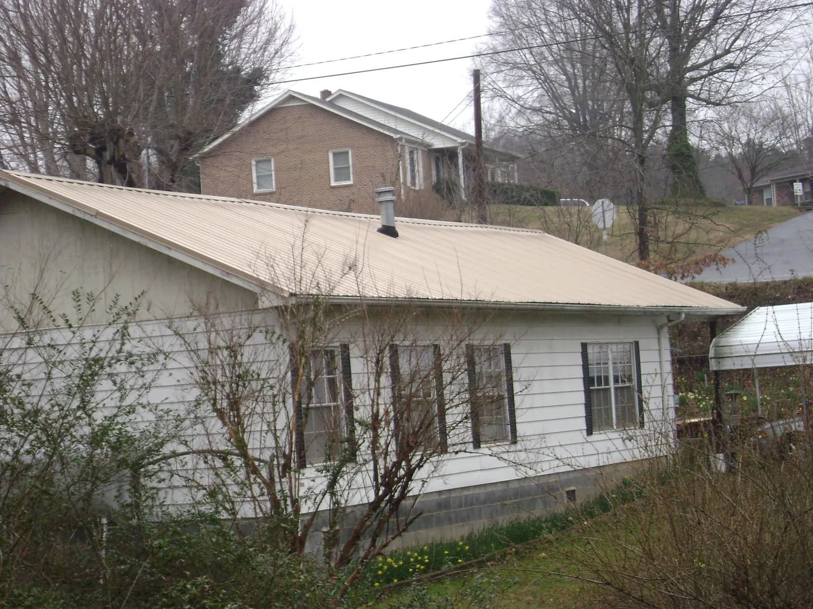 Tan metal roof on a white sided house set into a hillside — Commercial Roofing by Roofing Brothers in Hyannis Port